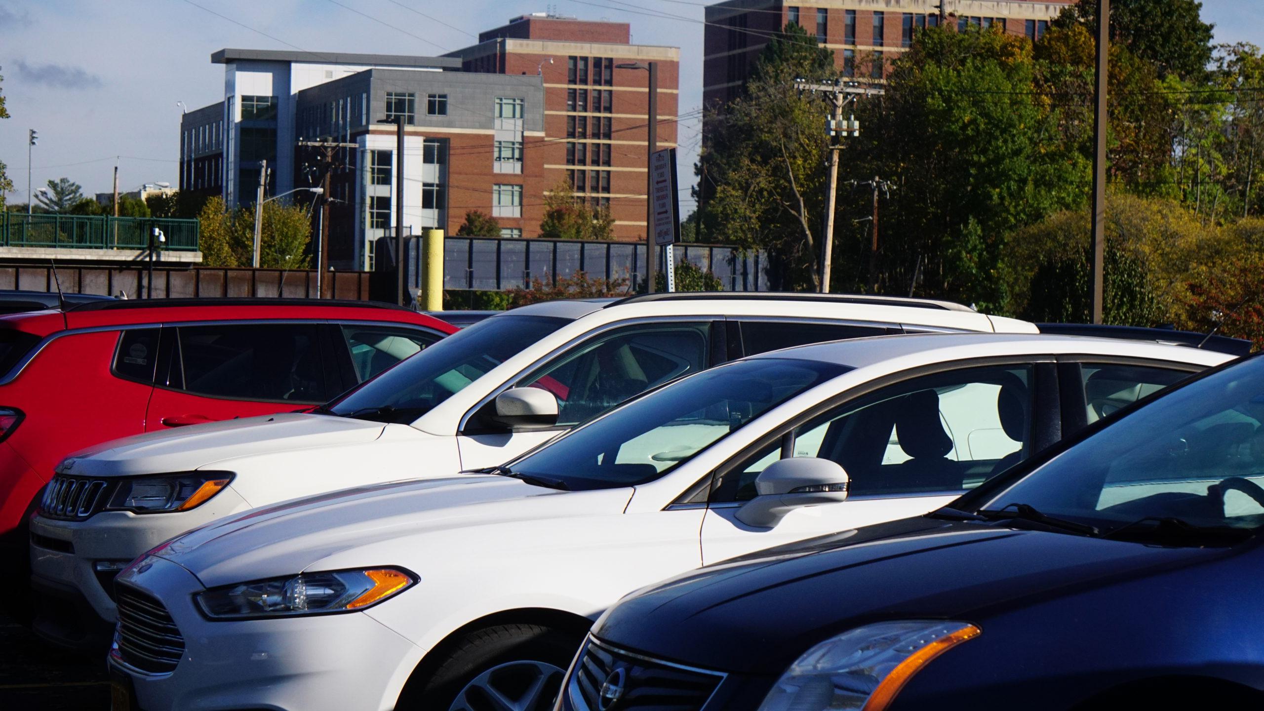 Vehicles parked in University of Rochester lot with brick buildings in background